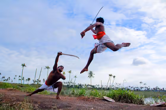Malayali — Two Kalaripayattu swordsmen demonstrating sword against sword mock combat in open air in rural Kerala, their shields can be seen left on the ground.