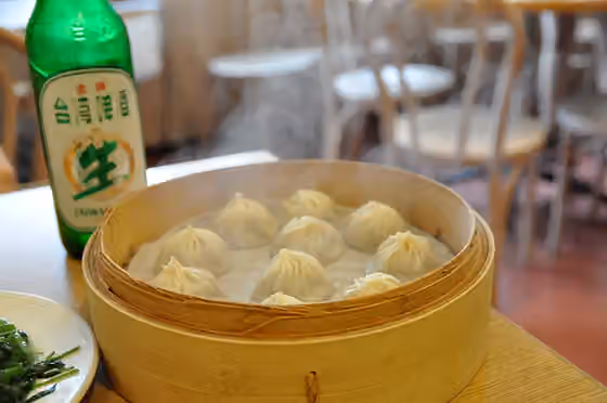 Masakan Taiwan — ​餐桌上的小籠包、炒空心菜與一瓶金牌台灣啤酒，在台北一家鼎泰豐餐廳內
