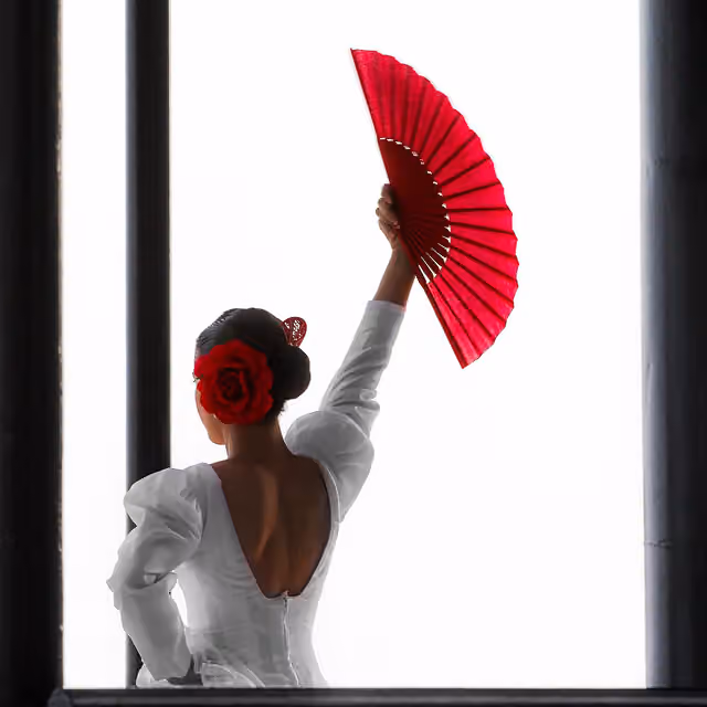 Penari flamenco berbaju putih mengangkat kipas merah.