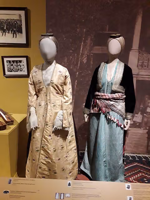Dua manekin mengenakan busana panjang bermotif dan selendang di ruang pamer museum.